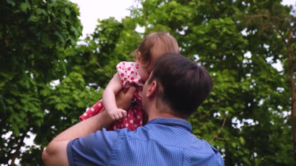 Táta je drží malou dcerou v letním parku. Táta hraje s malým dítětem, odhazuje dítě je šťastné a směje se. Zpomalený pohyb. — Stock video