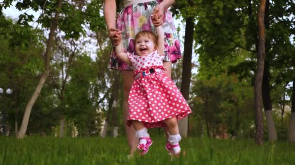 Bebé está girando en el aire en las manos de las mamás y se ríe. Hijita juega con su madre en la hierba verde en el parque en la primavera . — Vídeos de Stock