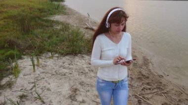 Kız kumsalda yürür ve mail online tablet denetler. kum yanında su üzerinde yürümek ve tablette müzik dinlerken kulaklık ile kız