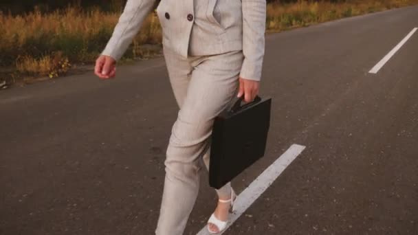 Slanke zakenvrouw met zwarte werkmap in haar hand is geasfalteerde wegen. meisje in een lichte pak en witte schoenen is op haar weg naar werk — Stockvideo