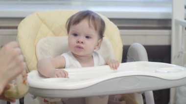 Çocuk mutfak sandalyesi üzerinde oturan kaşık yulaf lapası yiyor.