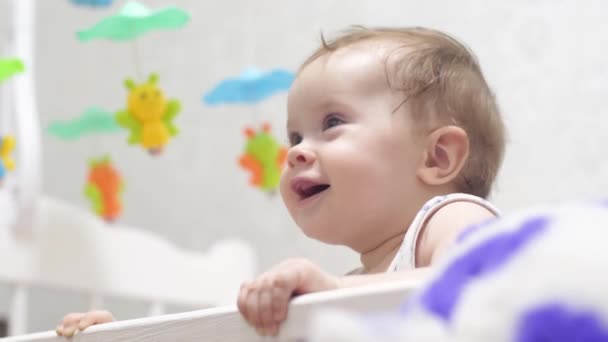 Small child stands on his feet in a baby bed. cute baby laughs — Stock Video
