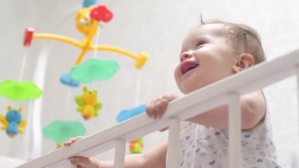 Bebé se para en las piernas en la cama, salta y ríe . — Vídeos de Stock