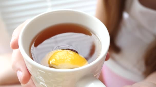 Chica bebe té caliente con rodaja de limón sentado en el alféizar de la ventana y sonríe . — Vídeos de Stock