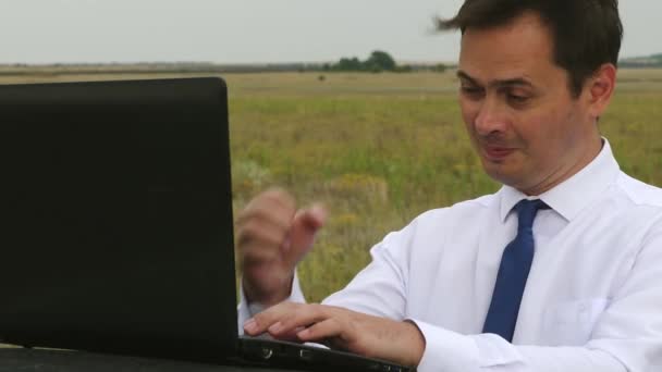 Uomo d'affari in camicia bianca e cravatta sta lavorando in campo sul computer sul tetto dell'auto — Video Stock