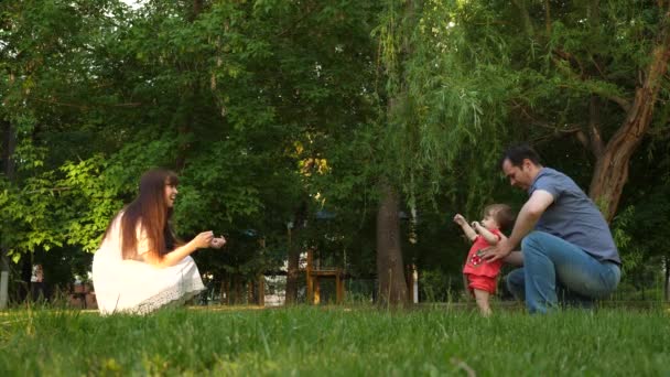 Barnet tar första stegen med hjälp av mamma och pappa på gräsmatta gräs. — Stockvideo
