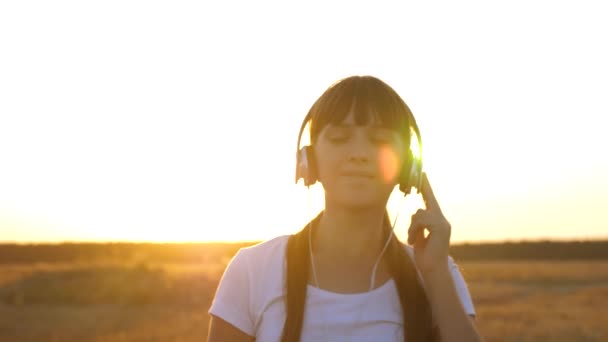 Hermosa chica en auriculares caminando por la carretera escuchando música y bailando — Vídeo de stock
