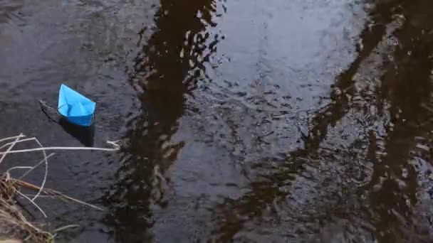 Piccola barca di carta blu che scorre con un flusso di fiume trasparente, riflesso in esso di alberi — Video Stock