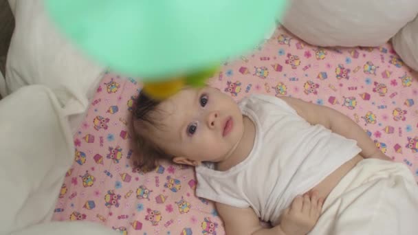 Pequena criança encontra-se no berço e olha para os brinquedos rotativos . — Vídeo de Stock