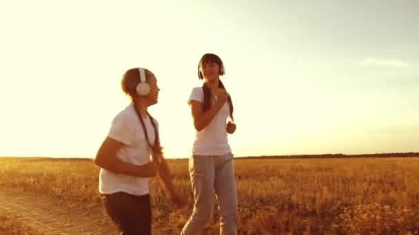 Niñas están entrenando al atardecer y escuchando música. adolescentes niñas en los auriculares haciendo deportes trotar en el campo . — Vídeo de stock