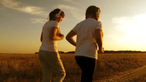 Teen girls in musical headphones playing sports in the countryside. young girls are practicing jogging at sunset and listening to music. — Stock Video