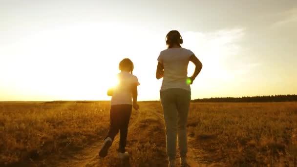 Chicas jóvenes están practicando jogging al atardecer y escuchando música. chicas adolescentes en auriculares musicales jugando deportes en el campo . — Vídeo de stock