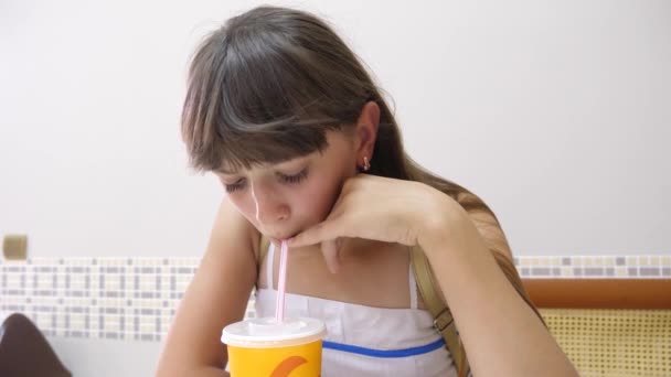 Dziewczyna siedzi przy stoliku w kawiarni i picia koktajl i uśmiechający się. — Wideo stockowe