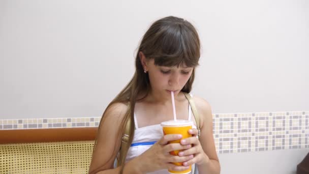 Jovem menina senta-se à mesa em um café e bebe suco e sorri . — Vídeo de Stock