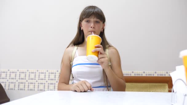 Молодая девушка отдыхает в кафе и пьет коктейль через соломинку — стоковое видео