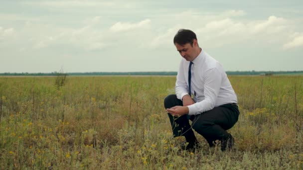 Агрономіст у білій сорочці та синій краватці розглядає поле. бізнесмен в полі думає про купівлю землі — стокове відео