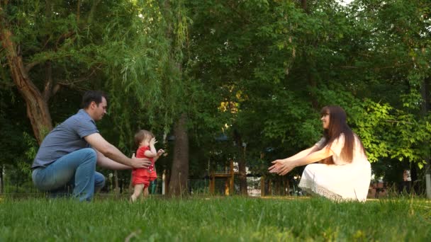 Pequeño bebé con mamá y papá aprende a caminar en un parque de verano — Vídeos de Stock