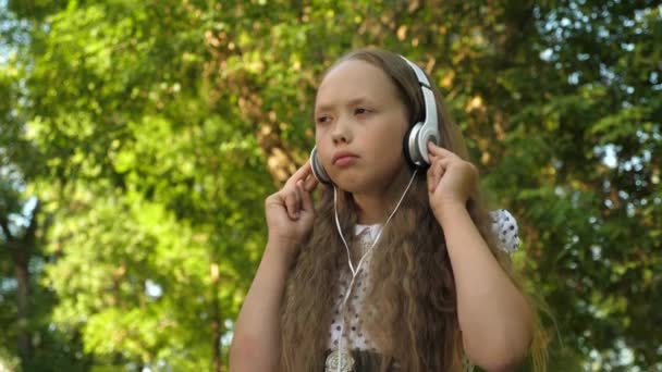 Chica triste con auriculares escuchando música en un parque de verano . — Vídeos de Stock