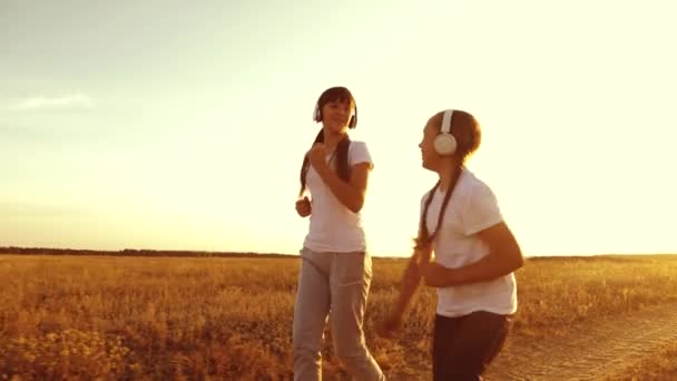 Niñas están entrenando al atardecer y escuchando música. adolescentes niñas en los auriculares haciendo deportes trotar en el campo . — Vídeos de Stock