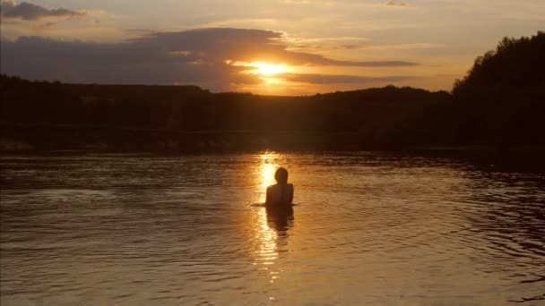 Menina fica na água e olha para o pôr do sol — Vídeo de Stock
