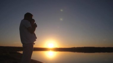 Babası küçük bebek akşam günbatımında kollarında tutar. Ağır çekim.