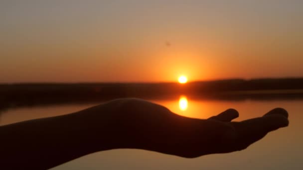 Manos sosteniendo el sol en las palmas, hermoso atardecer sobre el agua . — Vídeos de Stock