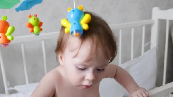 Petit bébé dans une couche avec les premières dents de lait se tient dans un berceau avec ses jouets et joue . — Video