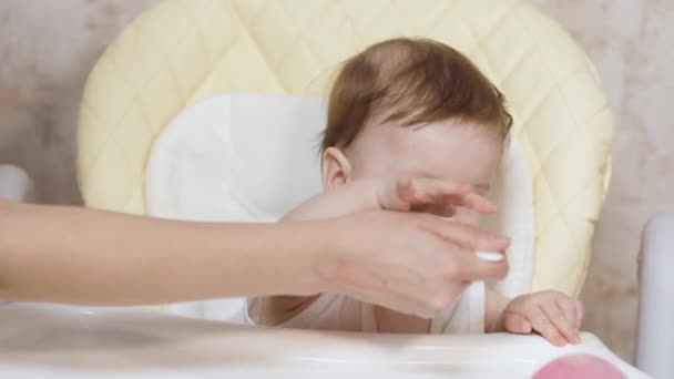 Mutter füttert Baby aus Löffel mit Kartoffelbrei, Baby frühstückt am Kindertisch. — Stockvideo