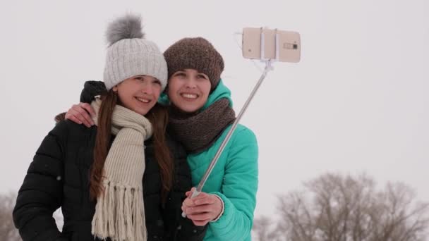 Mamá y su hija son fotografiadas en el teléfono inteligente, en el parque de invierno en la mañana de Navidad. Familia descansando en los bosques nevados, nieve blanca caerá . — Vídeos de Stock