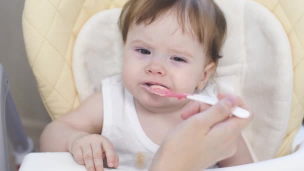 Mamá se alimenta de la cuchara de su pequeño hijo sentado en la trona de la cocina. primer plano — Vídeos de Stock