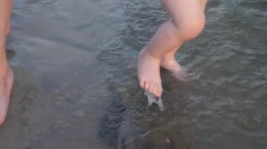 bebek bacakları su üzerinde gidin. Anne ve bebek sahilde yürümek. Yakın çekim. Ağır çekim.