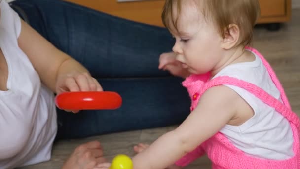 Mutter spielt mit kleinem Kind und sammelt bunte Ringe und Spielzeugpyramide im Kinderzimmer auf dem Fußboden — Stockvideo