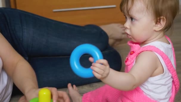 Mutter spielt mit kleinem Kind sie sammeln bunte Ringe und Spielzeugpyramide, kleine Tochter hält einen blauen Spielzeugring in der Hand — Stockvideo