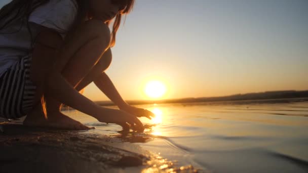 Девушка играет в ракушки в море на закате, замедленная съемка — стоковое видео