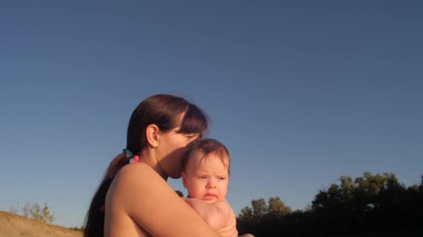 Mãe segura o bebê em seus braços e abraços contra o céu azul . — Vídeo de Stock