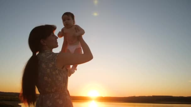 Moeder houdt kind in de armen van zon bij zonsondergang. Slow motion. — Stockvideo