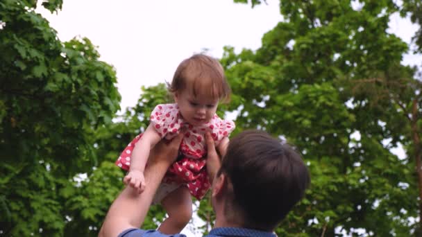 Папа играет с ребенком летом в парке. Маленькая девочка прыгает в воздух в руках папы и смеется. Медленное движение — стоковое видео