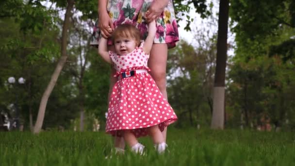 Mamá enseña a su hijita a caminar en el parque de verano en un césped verde . — Vídeos de Stock