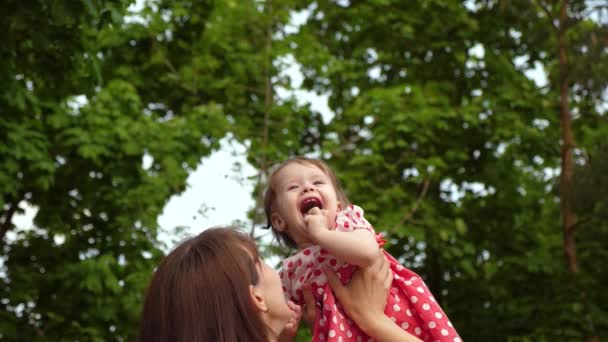 Маленькая девочка прыгает в воздухе в руках мамы и смеется. Мама играет со своей дочерью в летнем парке. Медленное движение . — стоковое видео