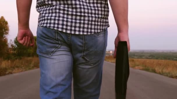 Férfi sétál egy fekete táska, aszfaltozott út mentén a kezében — Stock videók