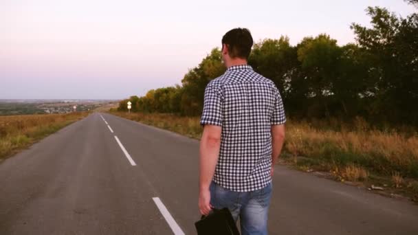 Joven empresario masculino está caminando por la carretera y llevando un maletín negro con documentos en la mano . — Vídeos de Stock