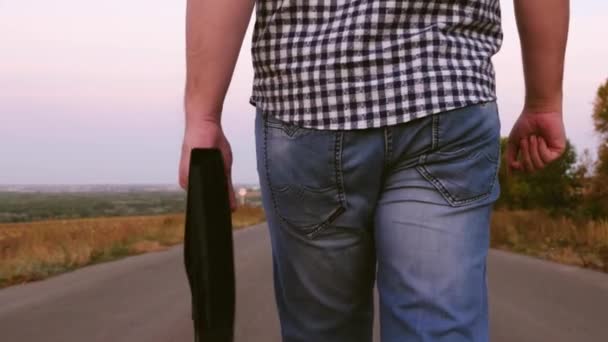 Joven empresario masculino está caminando por la carretera y llevando un maletín negro con documentos en la mano. primer plano . — Vídeos de Stock