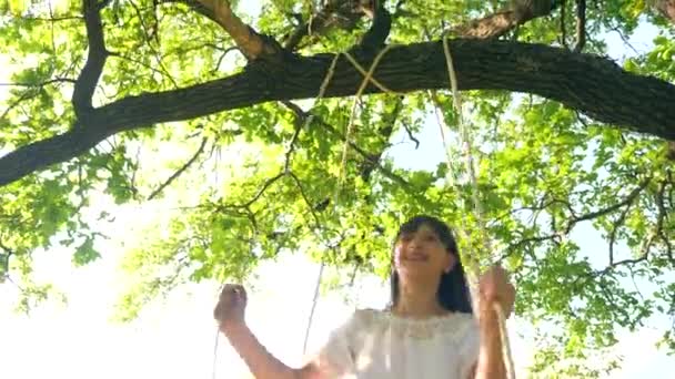 Girl is riding on swing in city park and smiling in glare of sunset — Stock Video