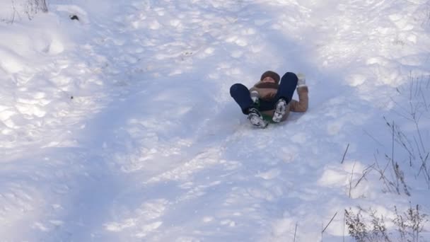 Gelukkig meisje is rollen neer sneeuw bedekte slee. meisje speelt in de winter in het park. Slow motion — Stockvideo
