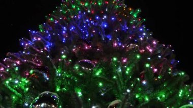 yüksek Noel köknar ağacı süslenmiş parlayan çelenk ve gece gökyüzüne karşı çok renkli topları. küçük kar düşüyor