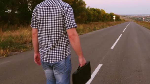 Joven empresario masculino está caminando por la carretera y llevando un maletín negro con documentos en la mano . — Vídeos de Stock