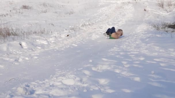 Dziewczyna toczy się na sanki z zjeżdżalnią wysoka pokryte śniegiem. dziewczyna gra w zimie w parku. Zwolnionym tempie — Wideo stockowe