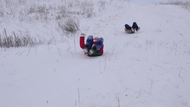 Счастливые дети скользят по снегу в санях с высокой горы. Девушки играют зимой в парке в рождественские праздники — стоковое видео