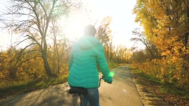 Flicka rider cykel på en asfalterad väg i höst park på bakgrunden av gula träd — Stockvideo