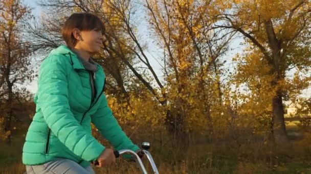 Chica monta una bicicleta en el parque de otoño en medio de álamos amarillentos — Vídeos de Stock